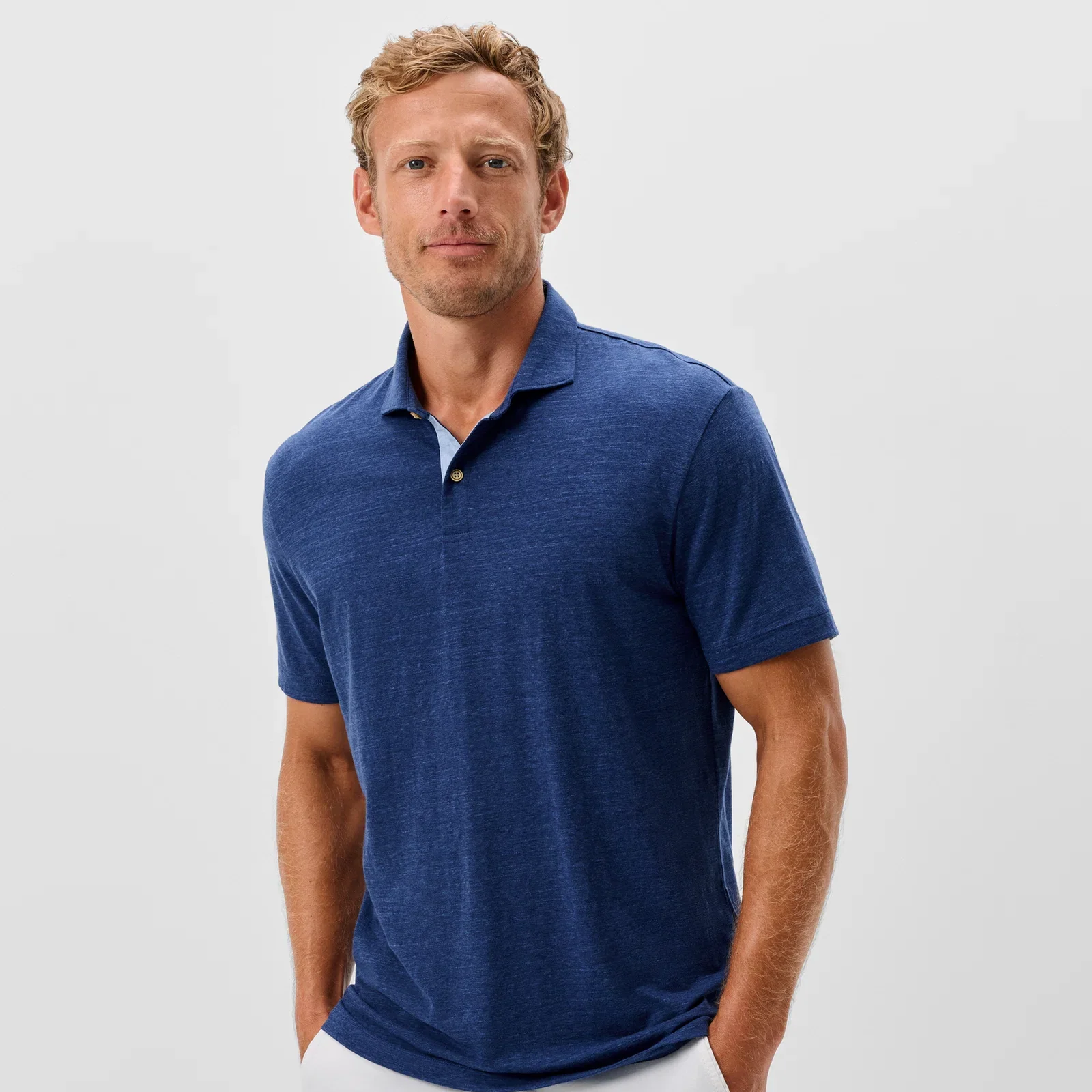 Man wearing a blue polo shirt and white pants on a light gray background
